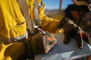 A man wearing yellow construction safety compliant gear holds a clipboard, indicating his role in a work-related environment.