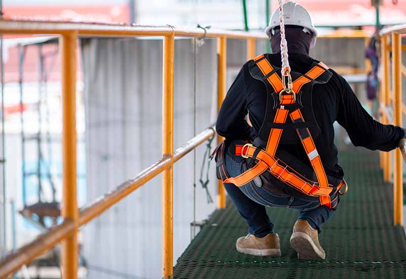 A man wearing an orange safety harness on a bridge, illustrating the critical need for safety measures against fall hazards in construction.