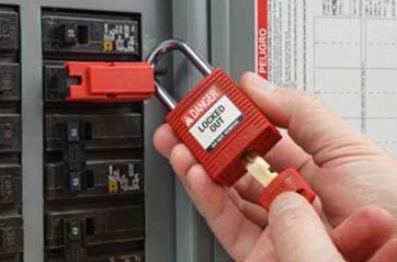 A person uses a key to unlock a padlock from a circuit breaker lockout.