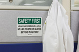 White lab coats hang next to a laboratory safety sign that indicates 'no lab coats or gloves beyond this point.'