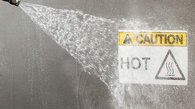 A pressure washer blasts a danger label.