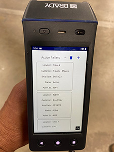 A hand holding a Brady HH83 RFID reader checking product locations for accurate tracking.